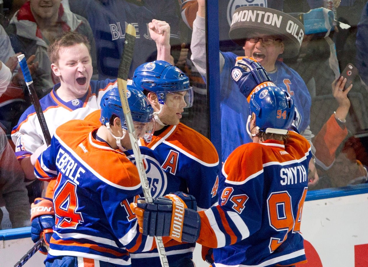 default-344 Three hockey players in orange-and-blue jerseys hug and celebrate while fans on the other side of the arena glass cheer wildly.